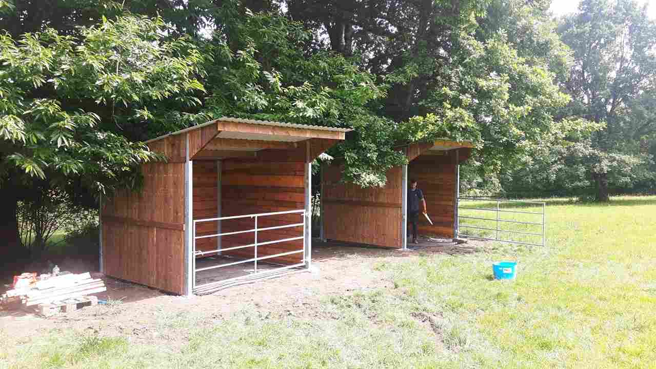 Deux abris pour chevaux en bois à ossature métallique alignés, vue de profil.