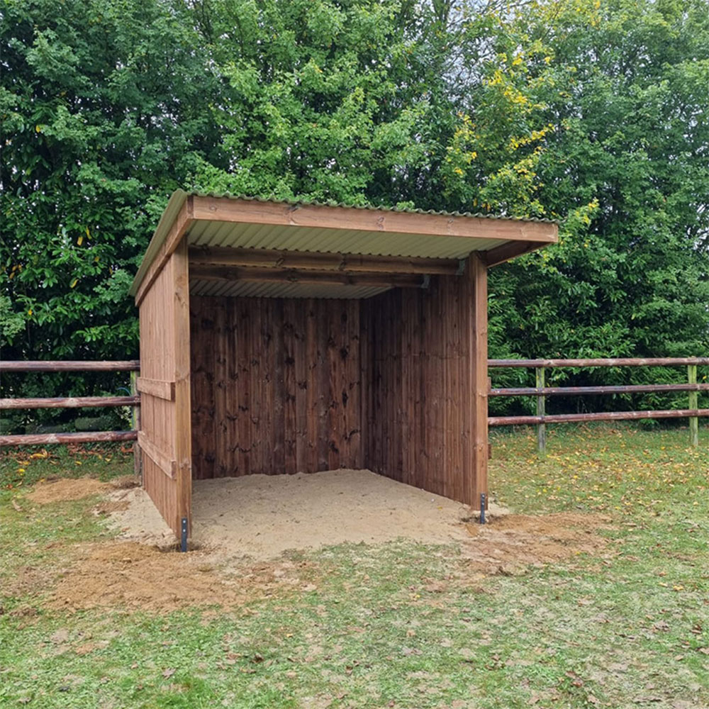 Abri chevaux en madrier, vue de près et de face, avec une clôture à 3 lisses en arrière-plan.