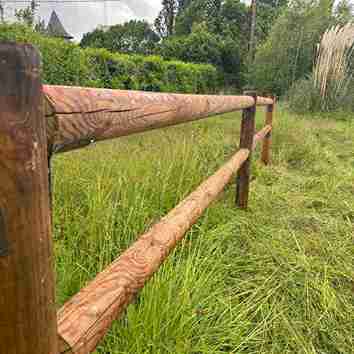 Clôture à deux lisses rondes en bois, vue en étant collé à la barrière de manière à faire apparaître les renforts.