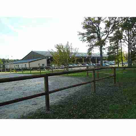 Clôture de carrière à 2 lisses en bois, installée à proximité d’une carrière et de chevaux.