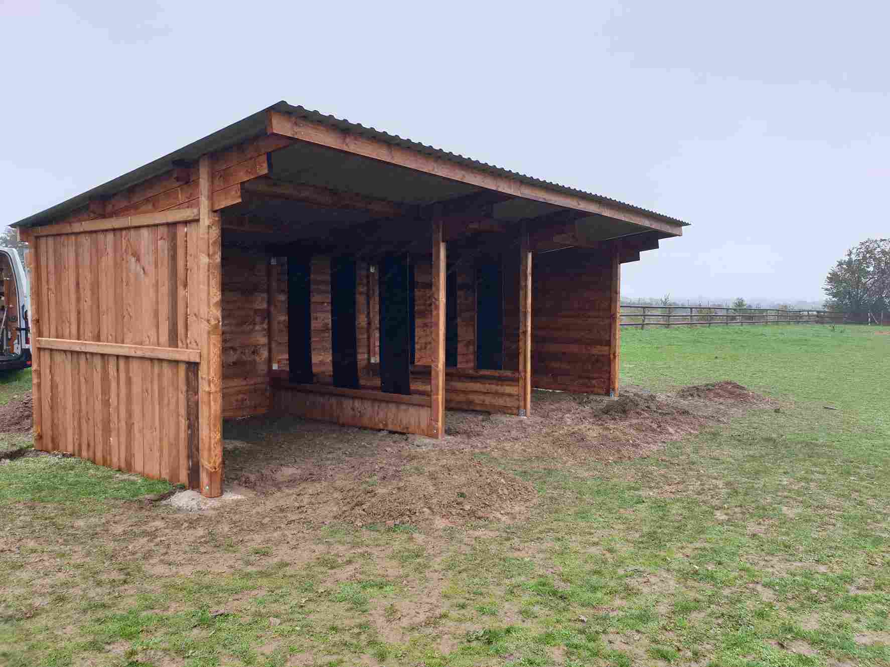 Double abri pour chevaux avec distributeur de foin central, vue de profil à mi-distance.