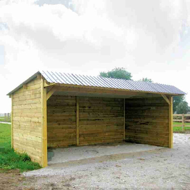 Abri pour chevaux en bois avec clins, toit double pente, vu de près et légèrement de profil.