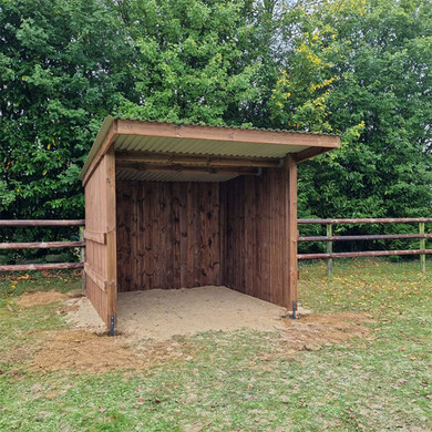Abri chevaux en madrier, vue de près et de face, avec une clôture à 3 lisses en arrière-plan.
