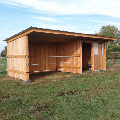 Abri box pour chevaux, vu de face et légèrement de profil, à côté d’une clôture HSW1.