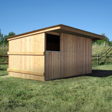 Box à bardage, vu de profil, à côté d’une clôture en bois et de bottes de foin.