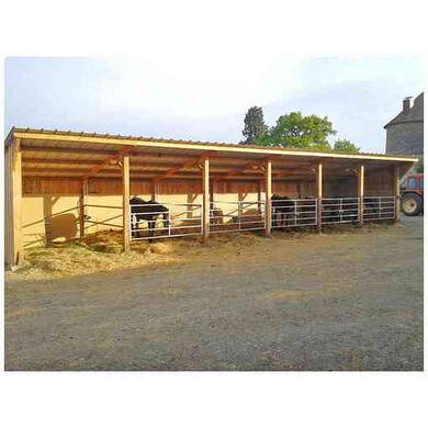 Hangar d’élevage pour chevaux, au milieu d’une propriété, vu de face à côté d’un tracteur.