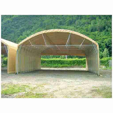 Tunnel de stockage en PVC, vu de face à mi-distance, avec une forêt en arrière-plan.
