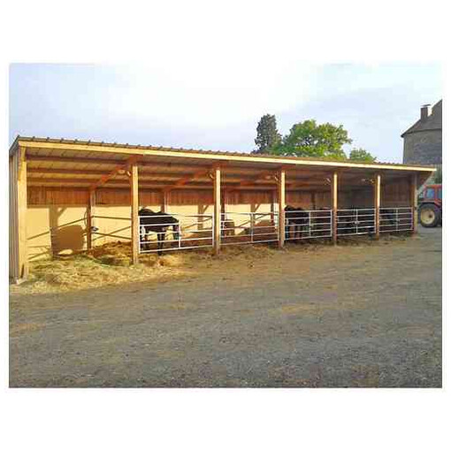 Hangar d’élevage pour chevaux, au milieu d’une propriété, vu de face à côté d’un tracteur.