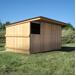 Box à bardage, vu de profil, à côté d’une clôture en bois et de bottes de foin.